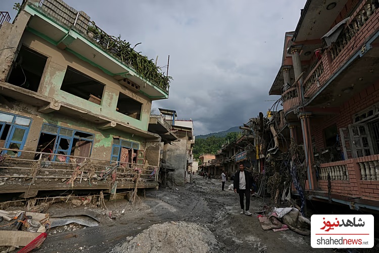 People walk along a street lined with damaged structures after flash flooding in the Devighat area of Nuwakot district in Nepal, 28 August, 2026 